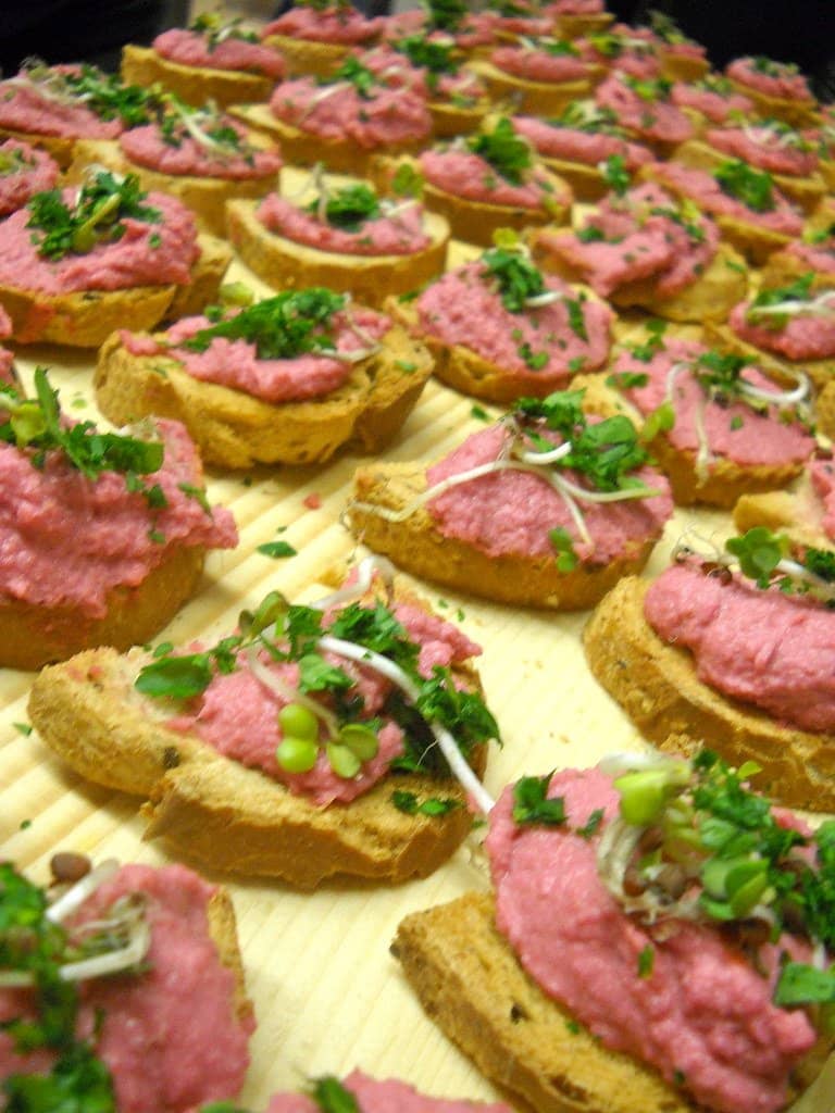 Toasted crostini spread with beetroot hummus and topped with microgreens
